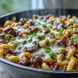 A steaming bowl of One-Pan High Protein Chili Mac topped with green onions, sour cream, and crushed tortilla chips.
