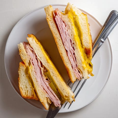 A pressed Cuban sandwich on a wooden board, showcasing melted Swiss cheese and dill pickles nestled between savory roast pork and ham.
