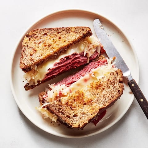 Golden-brown Reuben Sandwich halves on a cutting board, showcasing melted Swiss cheese, savory corned beef, and tangy sauerkraut oozing from buttery rye bread.