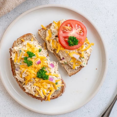A delicious open-faced Tuna Melt served hot with a side of dill pickles and mixed greens.