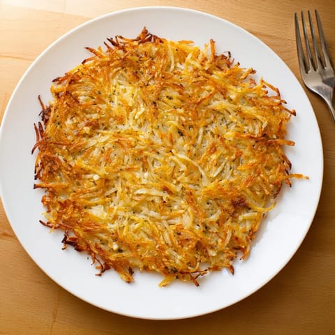 A close-up of perfectly crispy Hash Browns served alongside sunny-side-up eggs and bacon.