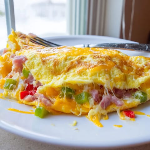 Golden Denver Omelet with melted cheddar, diced ham, and colorful bell peppers, folded perfectly on a white plate.