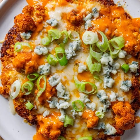 Slices of Buffalo Cauliflower Pizza on a white plate, featuring a crispy cauliflower base, spicy sauce, and optional blue cheese crumbles, perfect for a vegetarian main dish.  