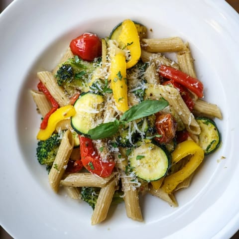A close-up of vibrant Pasta Primavera, featuring tender broccoli, yellow squash, and red onion, garnished with fresh basil and a bright squeeze of lemon.