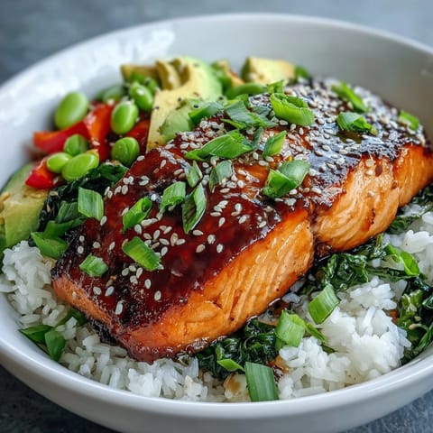 Tender soy-ginger glazed salmon fillets sit on fluffy white rice, garnished with green onions and sesame seeds.