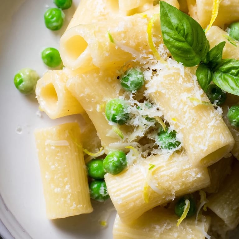 A close-up of pea and lemon ricotta pasta showcases rigatoni coated in creamy sauce, dotted with peas and a sprinkle of Parmesan.