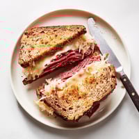 Golden-brown Reuben Sandwich halves on a cutting board, showcasing melted Swiss cheese, savory corned beef, and tangy sauerkraut oozing from buttery rye bread.