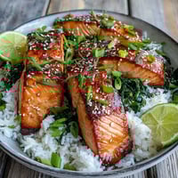 Golden-brown miso glazed salmon bowl with jasmine rice and sautéed spinach topped with sesame seeds and green onions.