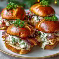 Miniature Kentucky Hot Brown sandwiches on brioche buns with turkey, bacon, and creamy Mornay sauce, baked until golden and topped with parsley.