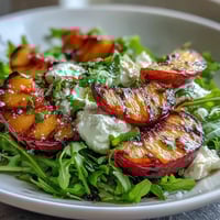 Grilled peaches and creamy burrata atop arugula, drizzled with honey and balsamic glaze for a sweet summer salad.